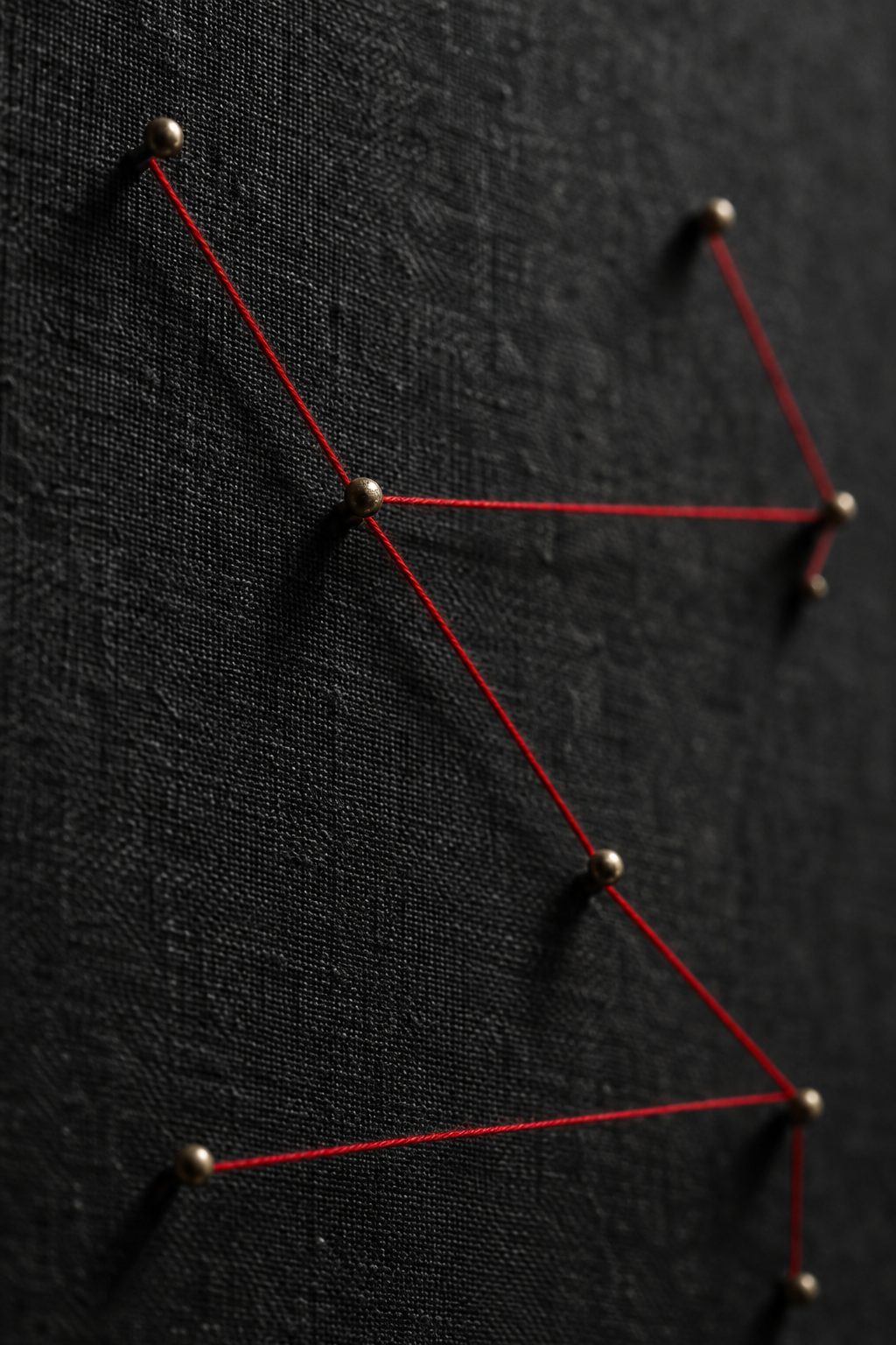 Red thread stretched between brass pins on a dark linen board